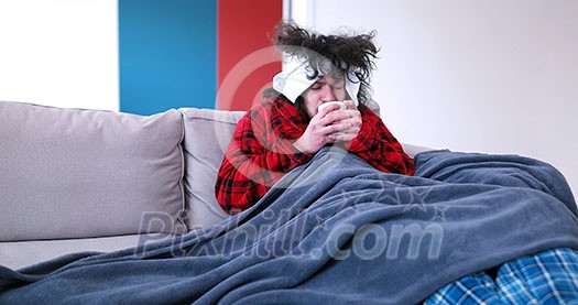 young Handsome sick man is holding a cup while sitting on couch covered in plaid