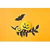 Black paper leaves branch, flying bat and pumpkin with a scary face on an orange background with space for text. Handcraft paper composition to Halloween. Flat lay
