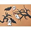 Creative composition of paper with flying bats and ghosts over tree branches on a brown background with space for text. Handcraft layout for Halloween. Flat lay