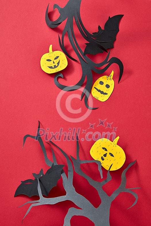 Halloween composition of handcraft paper pumpkins, bats and trees on a red background with copy space. Flat lay Halloween composition of handcraft paper pumpkins, bats and trees on a red background with copy space. Flat lay