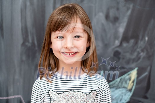 portrait of  happy smiling cute little girl standing in front of black chalkboard