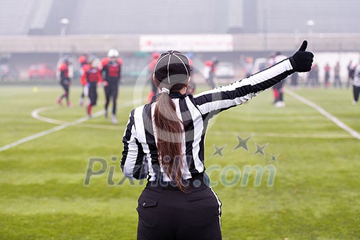 rear view of female american football referee giving signals to professional players during match on the stadium field