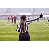 rear view of female american football referee giving signals to professional players during match on the stadium field