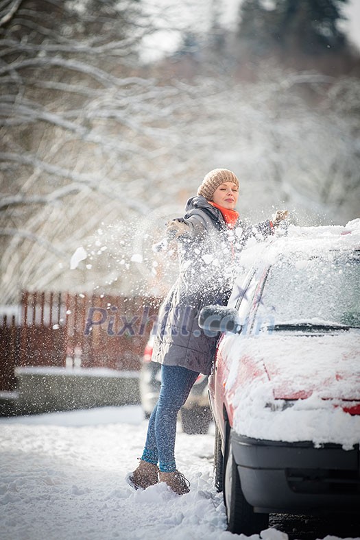 Pretty, young woman cleaning her car from snow after heavy snowstorm (color toned image) Pretty, young woman cleaning her car from snow after heavy snowstorm (color toned image)