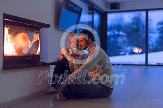 Young romantic couple sitting on the floor in front of fireplace,talking and drinking tea on cold winter night at home Young romantic couple sitting on the floor in front of fireplace,talking and drinking tea on cold winter night at home