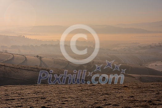 Beautiful winter landscape during sunset over snow covered field with fog and pollution in the valley behind