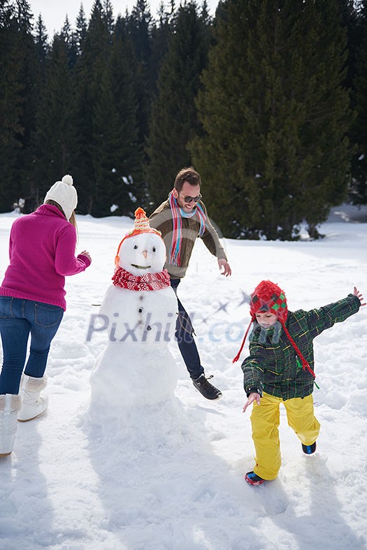 happy young  family playing in fresh snow and building snowman at beautiful sunny winter day outdoor in nature