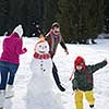 happy young  family playing in fresh snow and building snowman at beautiful sunny winter day outdoor in nature