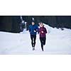 healthy young couple jogging outside on snow in forest. athlete running on  beautiful sunny winter day