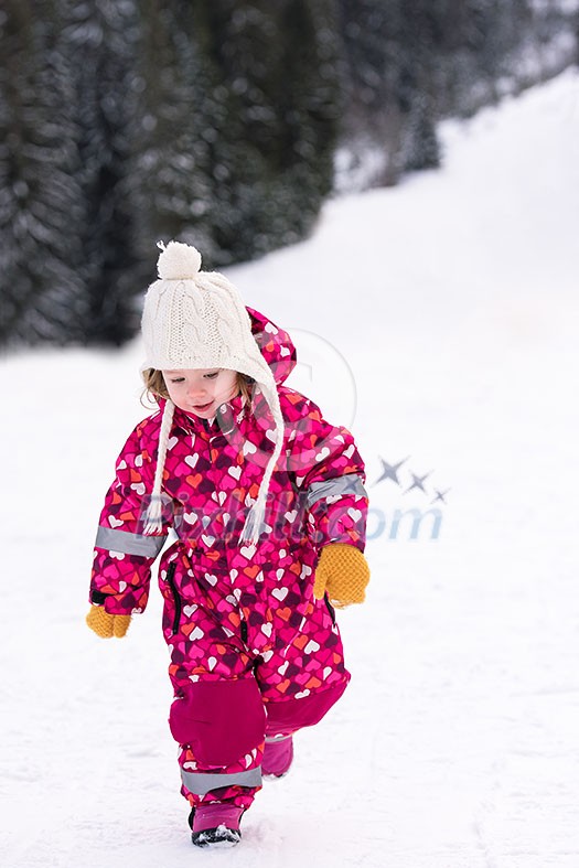 happy cute little girl wearing a red snow suit and white hat  while having fun and playing on fresh snow at snowy winter day