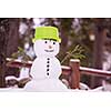 Happy smiling snowman with green hat and carrot nose standing in winter forest