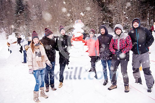 group portrait of young happy business people after a competition posing with finished snowman while enjoying snowy winter day with snowflakes around them during a team building in the mountain forest group portrait of young happy business people after a competition posing with finished snowman while enjoying snowy winter day with snowflakes around them during a team building in the mountain forest