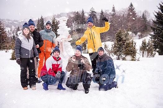 group portrait of young happy business people after a competition posing with finished snowman while enjoying snowy winter day with snowflakes around them during a team building in the mountain forest