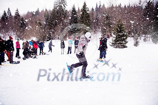 group of young happy business people having a running competition using snowshoes while enjoying snowy winter day with snowflakes around them during a team building in the mountain forest