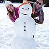 portrait of happy young couple with snowman at beautiful winter day with fresh snow and forest in background