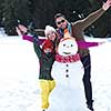 happy young  family playing in fresh snow and making snowman at beautiful sunny winter day outdoor in nature with forest in background