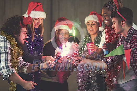 multiethnic group of young happy casual business people lighting a sparkler and having fun while celebrating new year eve in front of concrete wall at new startup office