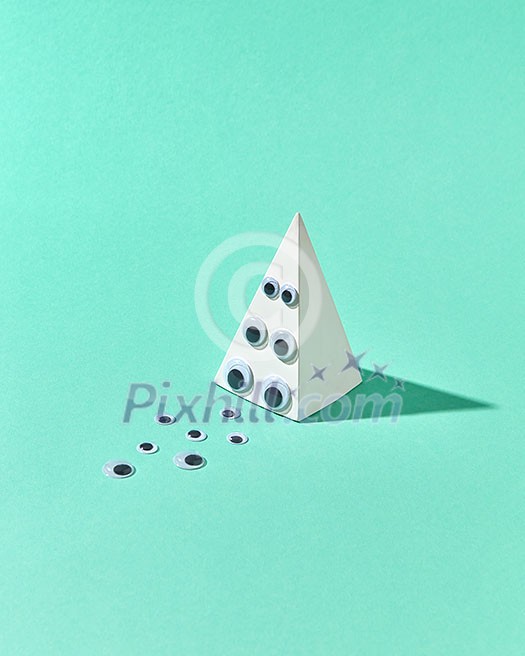 Geometric gupsum pyramid with eye pupils on a brink and on a light turquoise background with hard shadows and place for text. Halloween simbol of holiday party. Geometric gupsum pyramid with eye pupils on a brink and on a light turquoise background with hard shadows and place for text. Halloween simbol of holiday party.