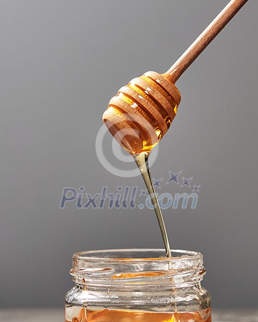 Sweet flower natural honey dripping into a jar and wooden spoon on a gray concrete background, copy space. Jewish rosh hashanah holiday concept.