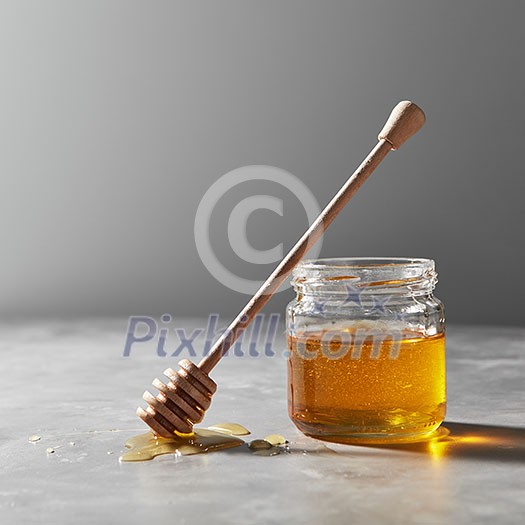 Wooden dipper in a puddle of syrup and a glass jar with fresh natural organic honey on a gray concrete background, place for text. Jewish New Year holiday concept. Wooden dipper in a puddle of syrup and a glass jar with fresh natural organic honey on a gray concrete background, place for text. Jewish New Year holiday concept.