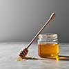 Wooden dipper in a puddle of syrup and a glass jar with fresh natural organic honey on a gray concrete background, place for text. Jewish New Year holiday concept.