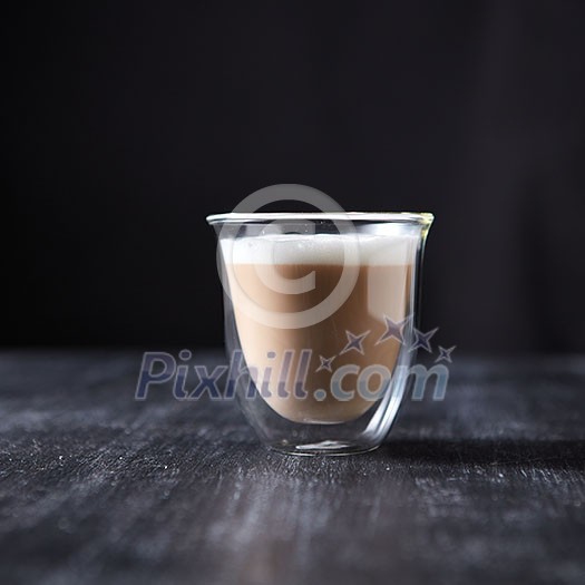 A glass cup of hot flavored cappuccino presented on a black wooden table with copy space. A glass cup of hot flavored cappuccino presented on a black wooden table with copy space.
