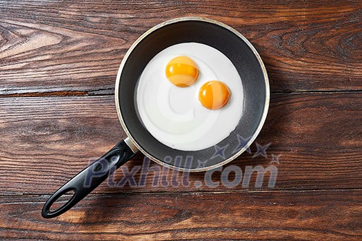 Fresh fried eggs with two yellow yoks in a frying pan on a wooden background, place for text. Breakfast healthy food concept. Flat lay. Fresh fried eggs with two yellow yoks in a frying pan on a wooden background, place for text. Breakfast healthy food concept. Flat lay.