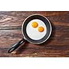 Fresh fried eggs with two yellow yoks in a frying pan on a wooden background, place for text. Breakfast healthy food concept. Flat lay.