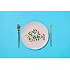 Many different pills and supplements as food on round white plate with fork and knife. Diet pills and supplements for dieting concept. Top view.