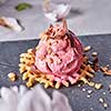 A scoop of berry ice cream on a wafer with chocolate chips on a slate plate on a gray concrete table decorated with petals flower. Sweet dessert