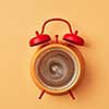 Vintage yellow alarm clock with red bells and cup of coffee on an yellow pastel background, place for text. Concept of morning coffee. Top view.