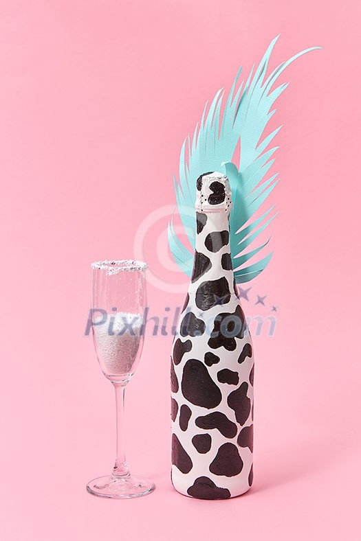 Holiday decorative composition of painted champagne bottle with black spots and paper cut tropical leaf with glass of white powder on a pastel millennial pink background, copy space. Holiday card.