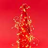 Shined Christmas lights string on a creative painted wine bottle on a red background with copy space. New Year congratulation card.