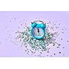 New Year alarm clock with almost twelve o'clock on a lavender background with holiday bright silver small stars tinsel, copy space.