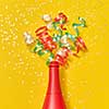 Holiday red painted wine bottle with multicolored paper srirals as a champagne bubbles on an yellow background, copy space. Flat lay.