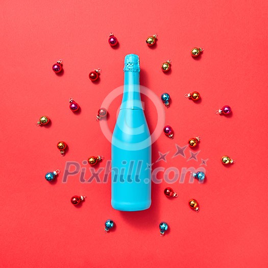 Decoration composition from blue painted bottle on a red background covered colorful glass New Year balls with copy space. Greeting holiday card