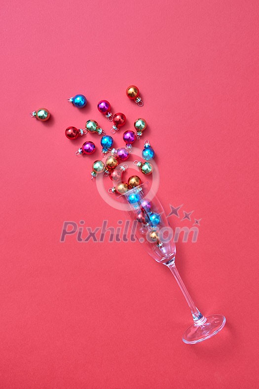 Christmas decoration balls in a glass as a champagne alcohol drink on a calypso coral background with plase for text. Greeting holiday card.