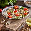 Appetizing homemade salad with fresh healthy ingredients - ripe vegetables, chicken meat in a ceramic plate with olive sause on a wooden background.