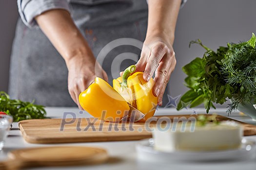 Woman housewife slices yellow pepper for salad on the kitchen table with greens and cheese. Step by Step Cooking Woman housewife slices yellow pepper for salad on the kitchen table with greens and cheese. Step by Step Cooking