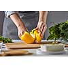Woman housewife slices yellow pepper for salad on the kitchen table with greens and cheese. Step by Step Cooking