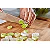 Slices of leek on a wooden board. Hands of the girl cut vegetables on the kitchen table. Cooking healthy food.
