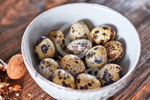 Fresh healthy quail eggs in a white bowl presented on a wooden table with a walnut. Dietary product. Top view Fresh healthy quail eggs in a white bowl presented on a wooden table with a walnut. Dietary product. Top view