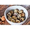 Fresh healthy quail eggs in a white bowl presented on a wooden table with a walnut. Dietary product. Top view