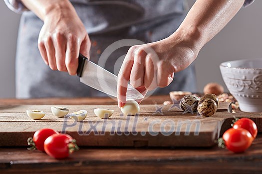 On a wooden table, the hands of a woman cut quail eggs on an old wooden board. Step by step salad preparation On a wooden table, the hands of a woman cut quail eggs on an old wooden board. Step by step salad preparation