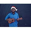 Indian man wearing Santa Claus Christmas red hat and playing Latin America traditional small guitar