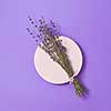 Decorative card with natural dry lavender bouquet on a ceramic round board and lilac background, copy space. Top view. Creeting card