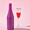 Glass of red wine with bottle painted hot pink with black spots and hard shadows on a pastel pink background, copy space.