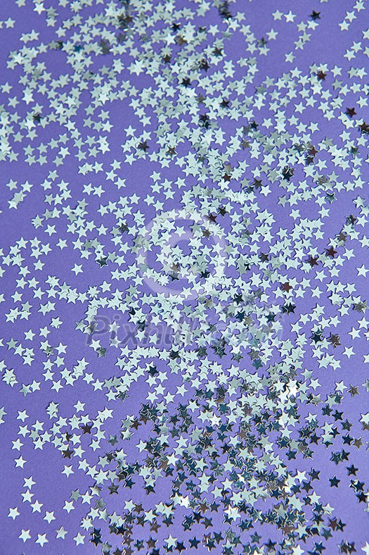 New Year decoration from bright small stars confetti on a lilac background. Holiday creative layout. Top view.