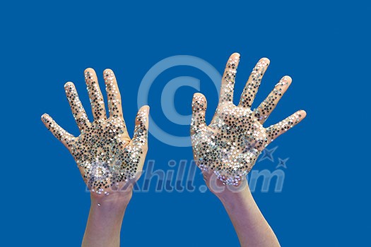 Creative composition of girl's hands with bright silver glitter small stars on a blue background, copy space.