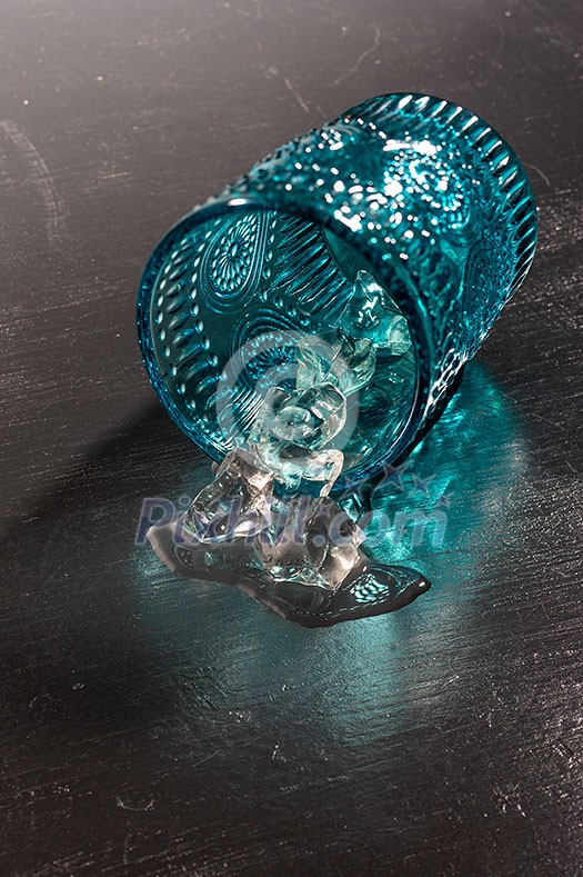 Melting ice in the ovetuned vintage blue glass on a wooden background with shadows, copy space.